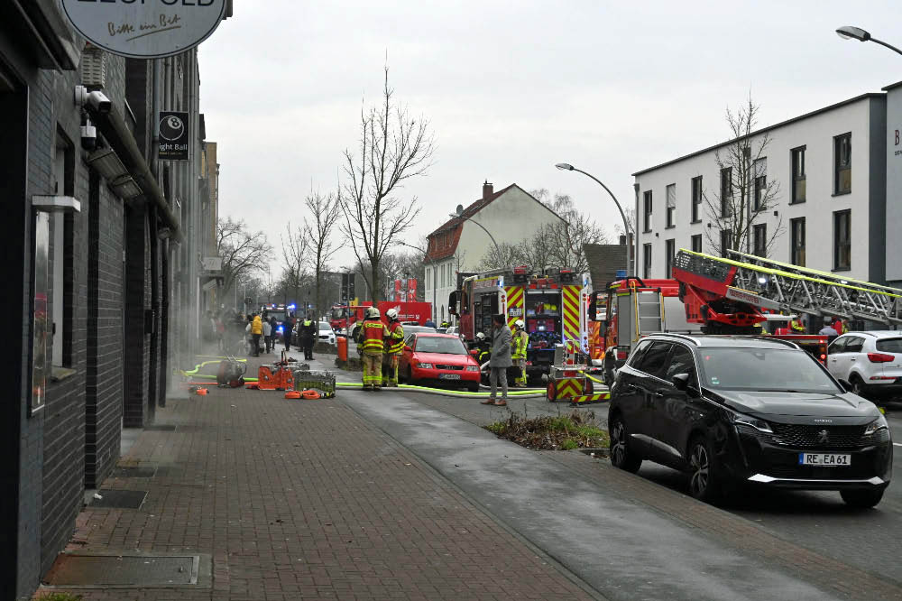 Dichter Rauch im Gebäude

Nach ersten Meldungen war die Feuerwehr zu einem gemeldeten Kellerbrand alarmiert worden. Vor Ort stellten die Einsatzkräfte jedoch eine deutlich verschärfte Lage fest. Dichter Rauch zog zeitweise durch das gesamte Gebäude. Mehrere Personen befanden sich im Haus und mussten gerettet sowie medizinisch versorgt werden. Die Feuerwehr leitete umgehend eine Menschenrettung ein und brachte die Bewohner ins Freie.

MANV der Stufe 10 ausgelöst

Aufgrund der Zahl der Betroffenen rief die Einsatzleitung einen Massenanfall von Verletzten der Stufe 10 aus. Damit wurde zusätzliche Unterstützung aus umliegenden Städten angefordert, um die Versorgung der Verletzten sicherzustellen.

„Wir sind zunächst von einem Kellerbrand ausgegangen. Vor Ort hat sich die Lage jedoch deutlich ausgeweitet“, erklärte Pressesprecher Jan Heppner. „Mehrere Personen mussten aus dem Gebäude gerettet und rettungsdienstlich versorgt werden.“

80 bis 100 Einsatzkräfte vor Ort

Nach Angaben der Feuerwehr waren im Verlauf des Einsatzes rund 80 bis 100 Kräfte von Feuerwehr und Rettungsdienst im Einsatz. Die starke Hitzeentwicklung im Keller erschwerte die Löscharbeiten erheblich. Mehrere Trupps gingen unter Atemschutz in das Gebäude vor.

„Wir rechnen damit, dass sich der Einsatz noch über mehrere Stunden hinzieht“, sagte Jan Heppner. Auch nach Abschluss der Löscharbeiten seien Nacharbeiten notwendig.

Straße gesperrt – Ursache noch unklar

Die Halterner Straße bleibt während des Einsatzes und der anschließenden Maßnahmen gesperrt. Zur Brandursache gibt es derzeit keine Angaben. Die Ermittlungen übernimmt die Polizei nach Abschluss der Löscharbeiten.