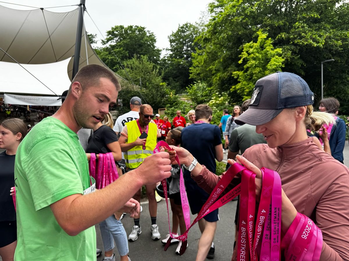 Helfer verteilen Medaillen und pinke Schleifen beim Dorstener Brustkrebslauf 2026